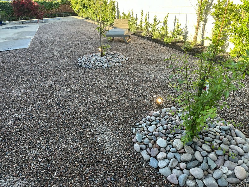 Decorative gravel landscape design for a small backyard with river rock accents, lighting, and drought-tolerant landscaping.
