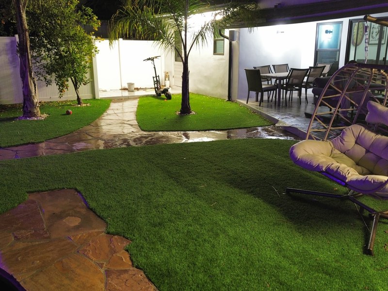 Small backyard artificial turf and patio lighting design with modern outdoor seating and landscape lighting.
