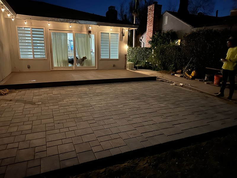 Small backyard paver patio and elevated deck remodel with outdoor lighting and modern entertainment space at night