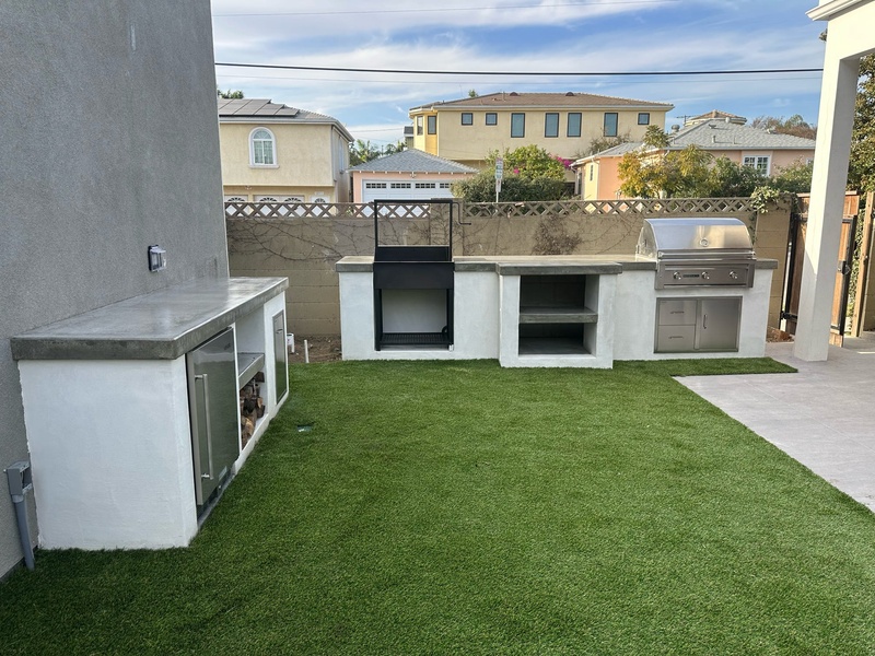 Completed custom outdoor kitchen with BBQ grill, pizza oven, refrigerator, and artificial turf